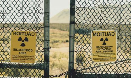 Fence with radiation warning signs and desert landscape in background